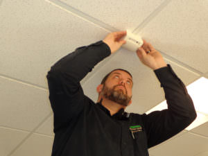 Technician Adam finishes installing a glass break sensor on a drop ceiling