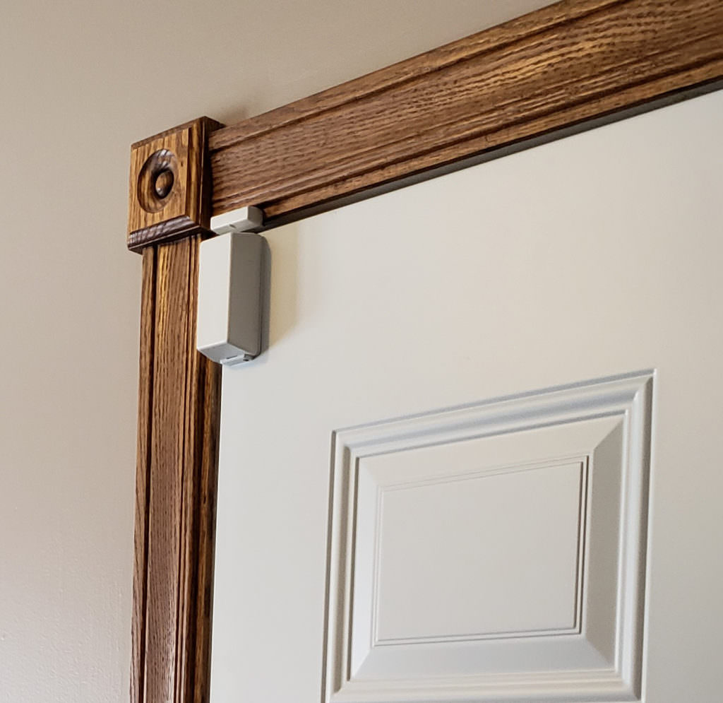 picture of a white door sensor on a white door with a brown door frame