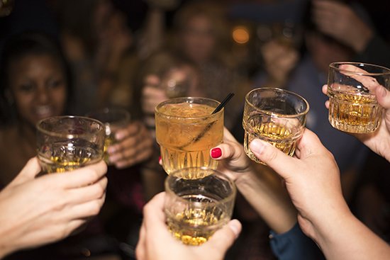 Picture of multiple hands raising whiskey glasses together in a toast