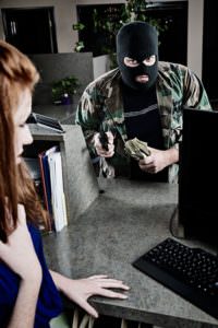 picture of a robber taking money from a scared bank teller