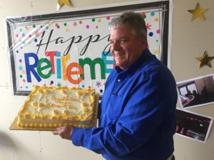 Tom Marthaler holding his cake while in front of a Happy Retirement banner