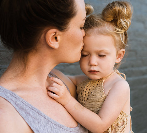 mother holding daughter and kissing her forehead