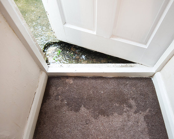 Open door with water on one side and wet carpet on the other