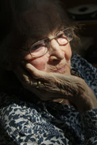 older woman with face bathed in sunlight holding her head in her hand