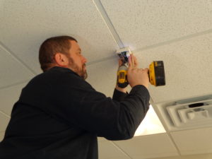 Technician Adam screws a glass break sensor onto a drop ceiling