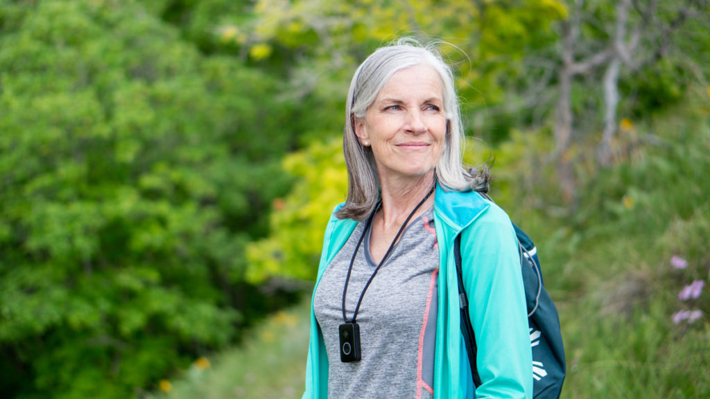 woman with gray hair wearing Belle medical alert pendant on a lanyard while hiking