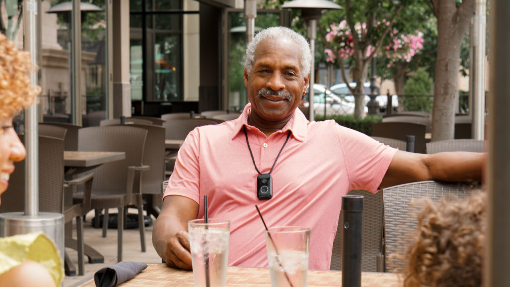 picture of a man with gray hair wearing a Belle medical alert pendant while seated at an outdoor table at a restaurant