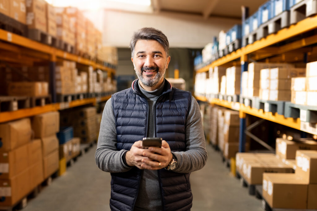 Man looking at camera in a warehouse holding a phone.