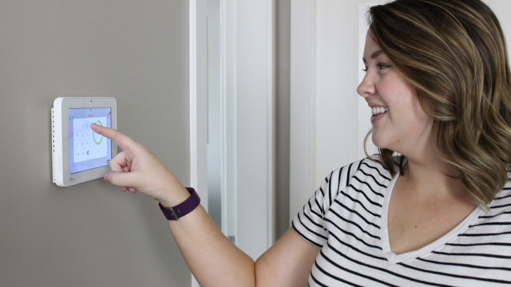 Woman smiling while looking at security panel and pressing a button on the panel.