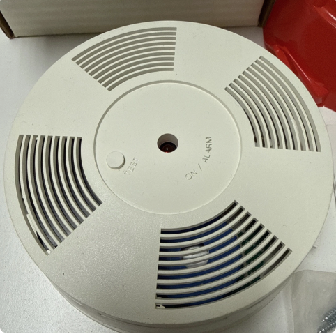 A circle-shaped, white security alarm unit with a button labeled "TEST"