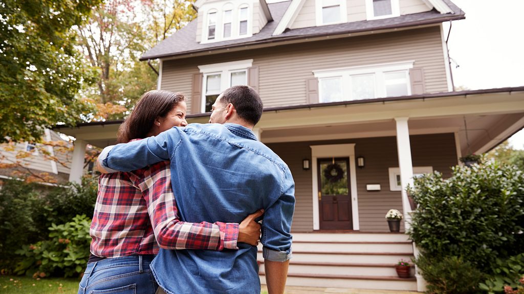 two young adults in a hug stand in front of their home
